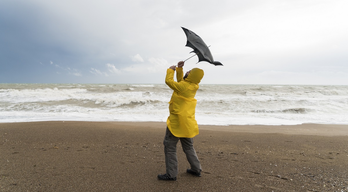 Man at the beach with a yellow rain jacket holding on to his umbrella in the wind