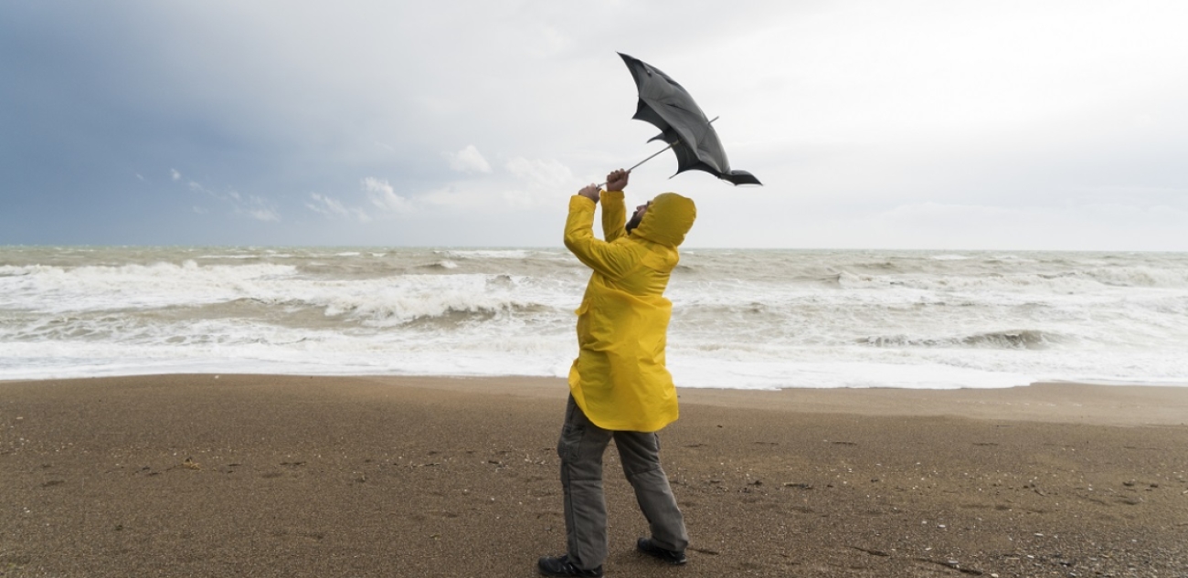 Homme sur une plage avec une veste de pluie jaune tenant son parapluie dans le vent